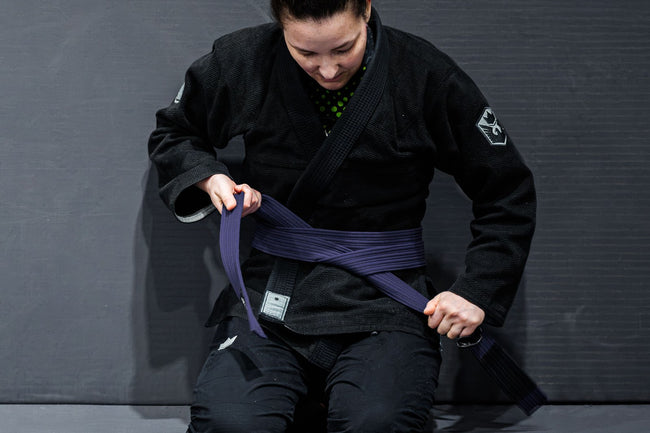 BJJ practitioner tying a purple belt during training | Forca Method