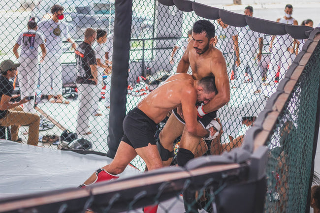 Two fighters grappling inside an MMA cage, applying ground control | Forca Method